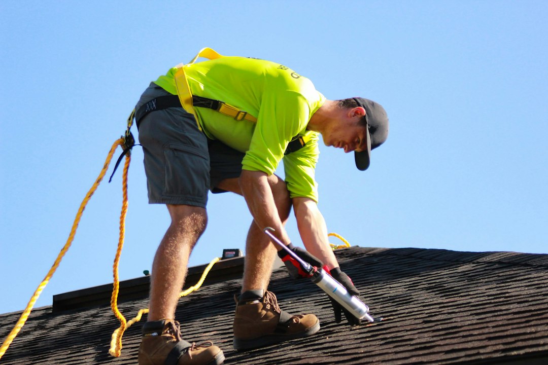 Professional roofing contractor installing shingles on residential roof with safety equipment